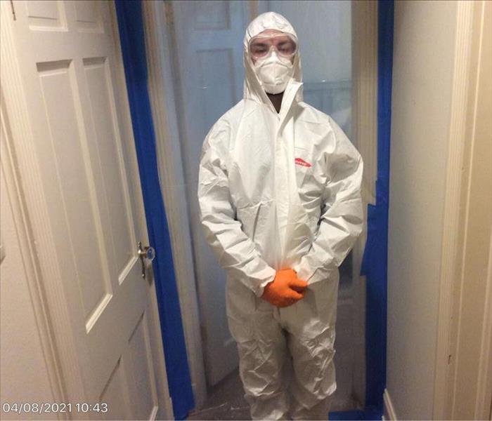 SERVPRO technician in PPE in front of a doorway with containment 