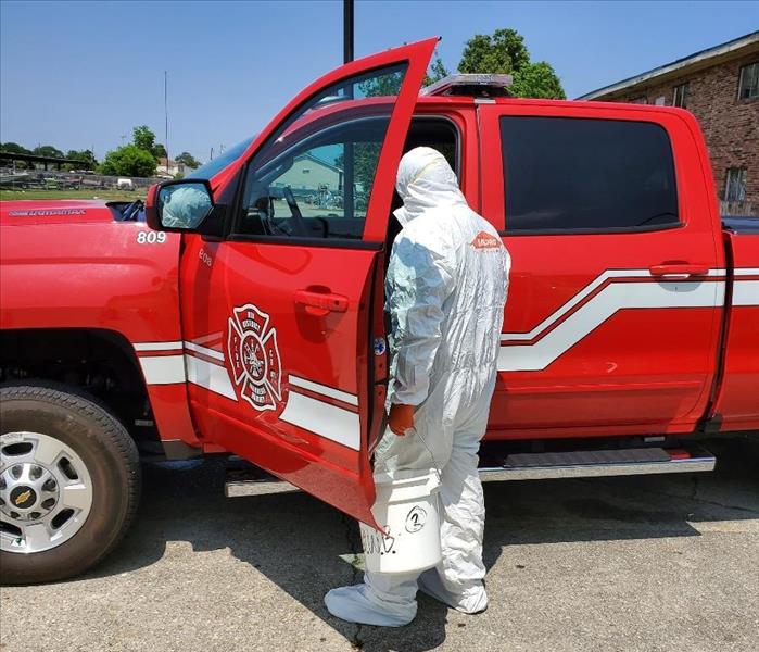 employee in white protective suite cleaning a red truck