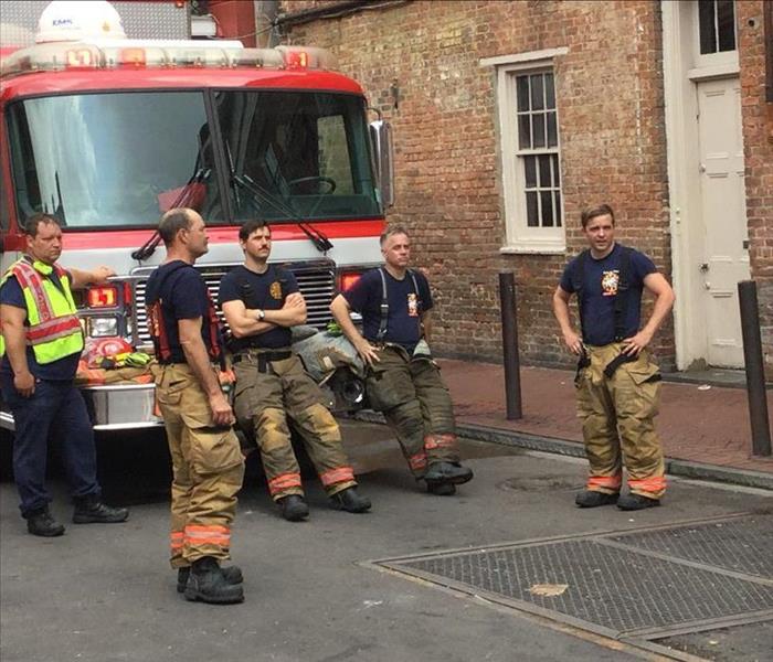 Firemen Hanging out by a Fire Truck in front of the FireHouse